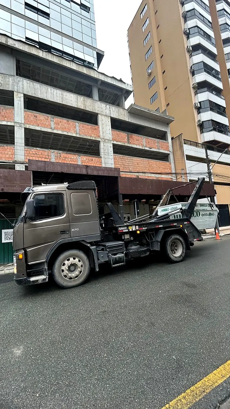 Caminhão da Eco Entulhos transportando caçamba em frente a uma obra